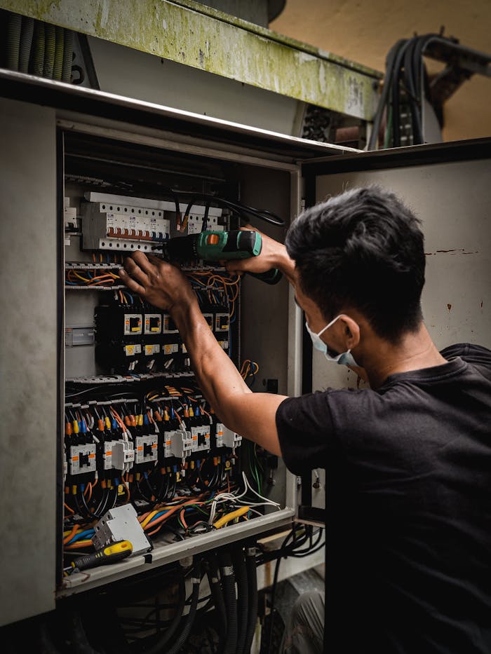 mission-img Technician working on circuit breaker panel, adjusting electrical wires indoors.